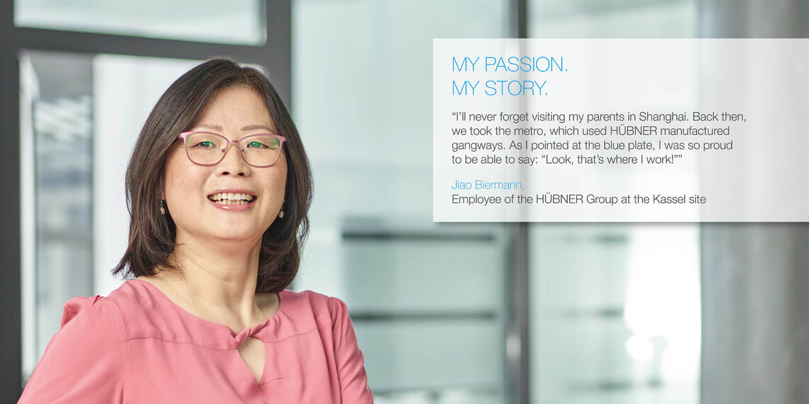 Mitarbeiterin im Büro mit Zitat (auf englisch): "I'll never forget visiting my parents in Shanghai. Back then, we took the metro, which used HÜBNER manufactured gangways. As I pointed at the blue plate, I was proud to be able to say: 'Look, that's where I work!'" Jiao Biermann, Employee of the HÜBNER Group at the Kassel Site